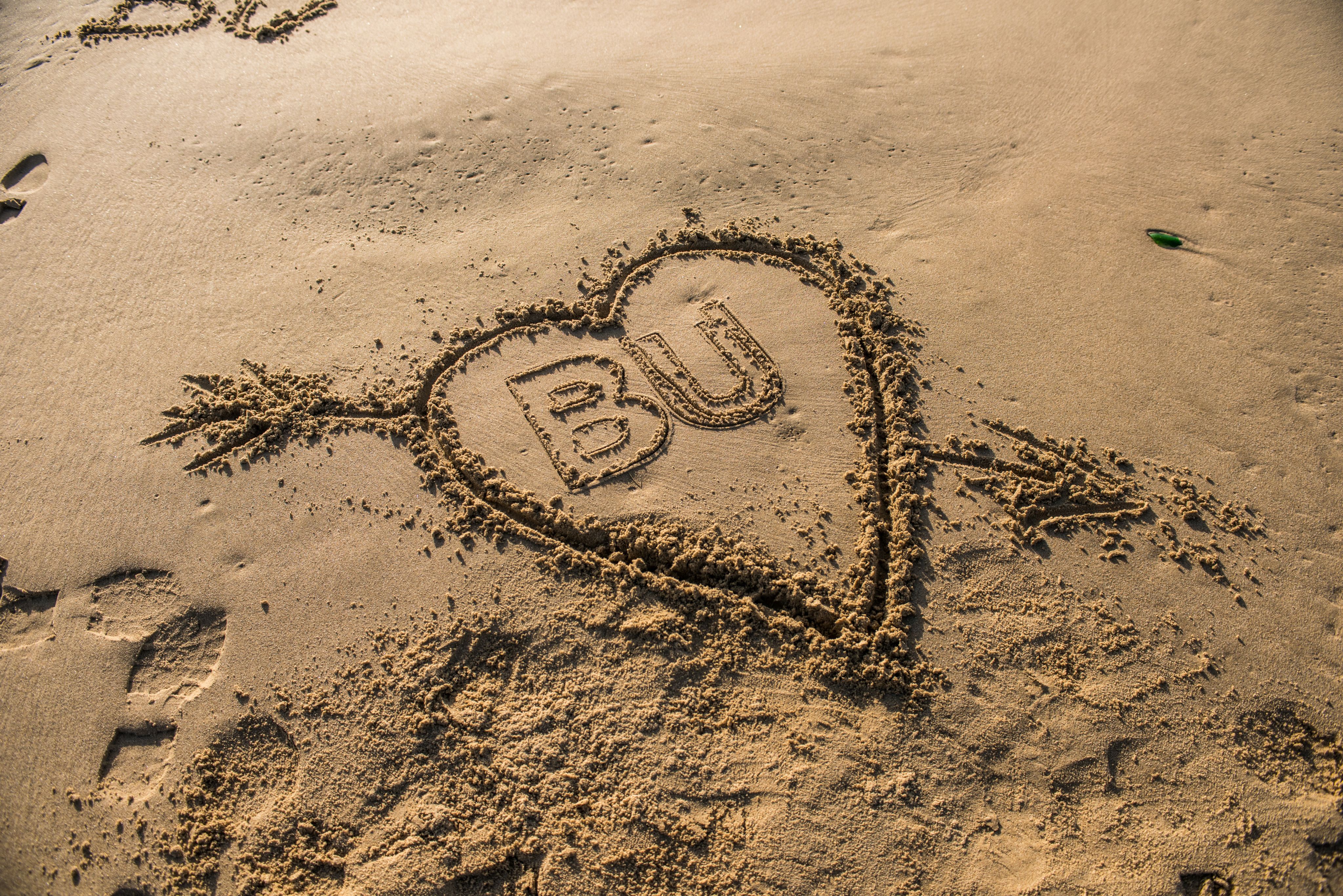 BU written in the sand surrounded by a heart
